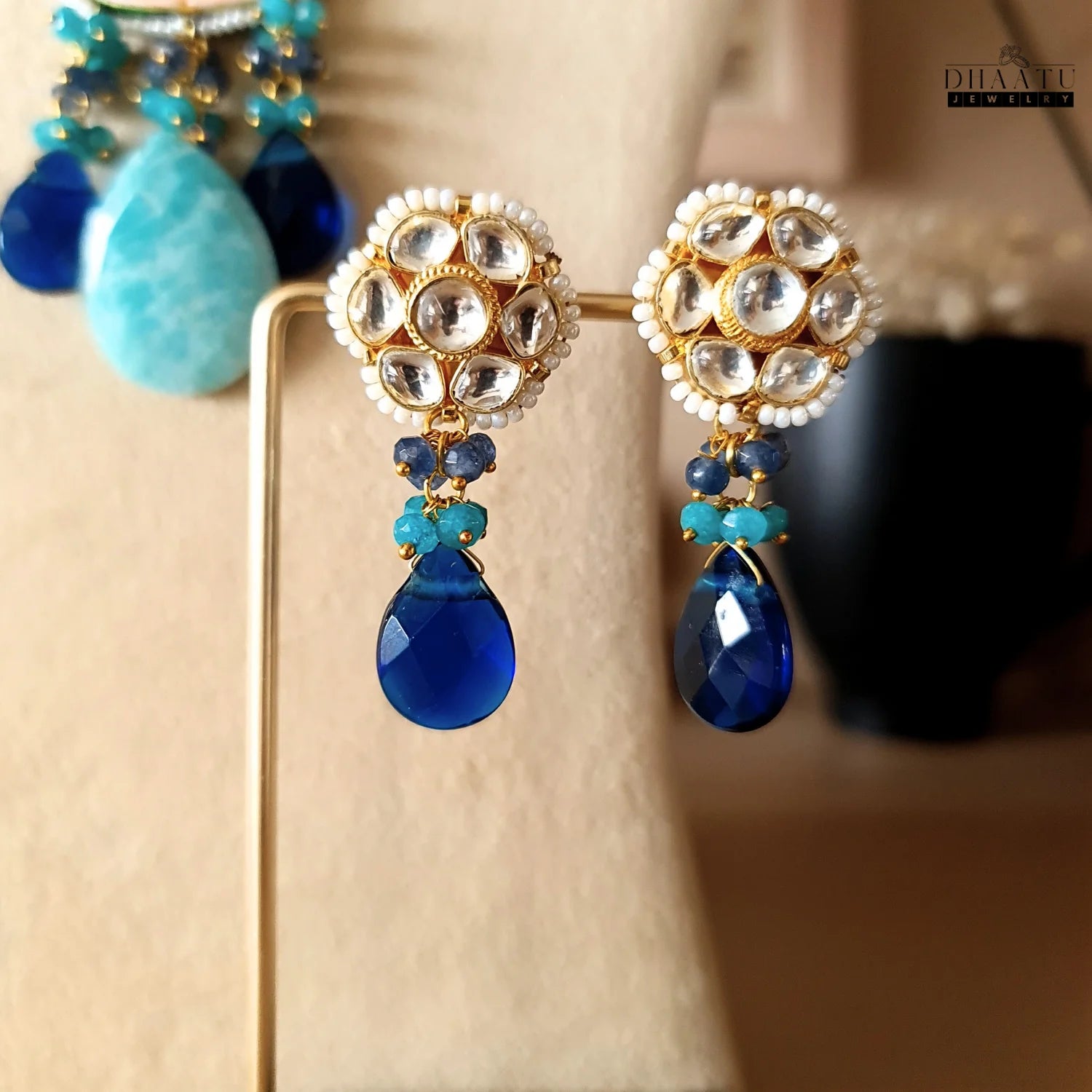 Close-up of Dhaatu Jewelry earrings, showcasing their traditional polki setting with white beads, and modern blue and turquoise gemstone drops, perfect for festive wear