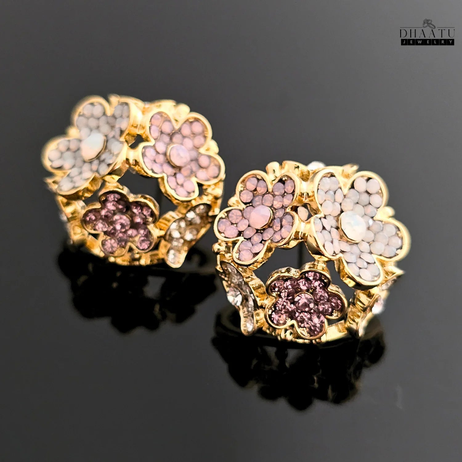 A pair of rose gold-plated floral stud earrings with multicolored crystals on a black reflective surface.
