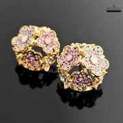 A pair of rose gold-plated floral stud earrings with multicolored crystals on a black reflective surface.