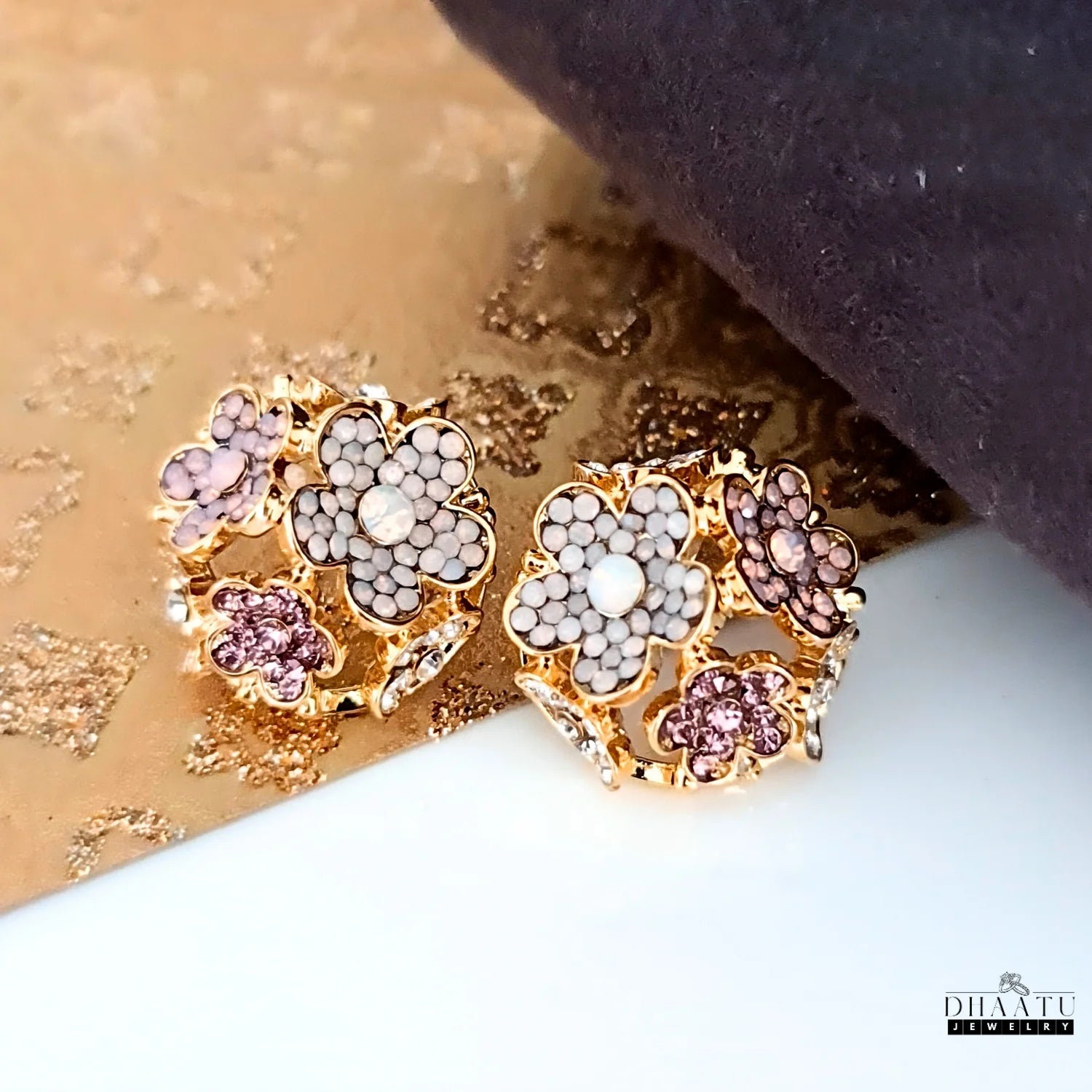 Rose gold-plated floral stud earrings with multicolored crystals on a golden and white background