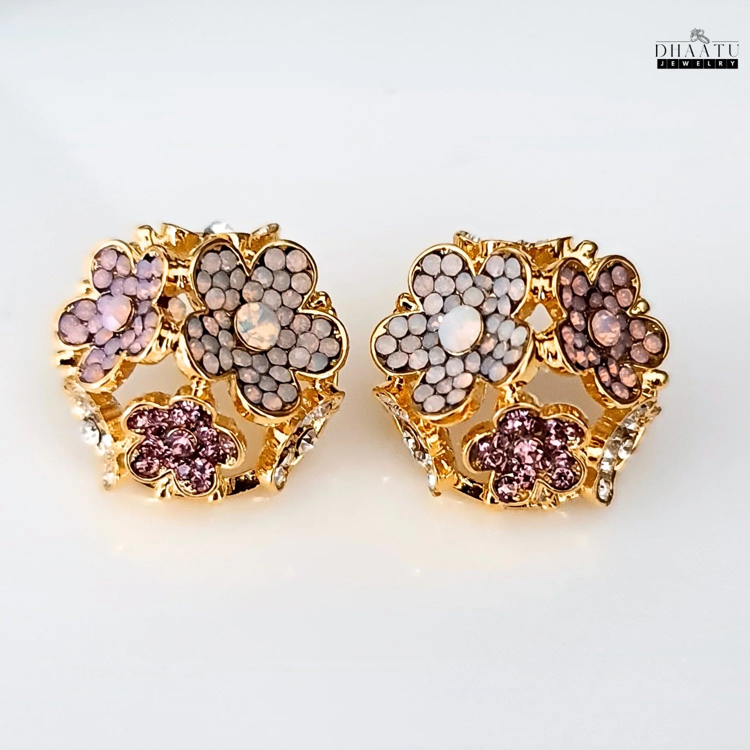 A pair of floral stud earrings with rose gold plating and pink, mauve, and white crystals on a white background.
