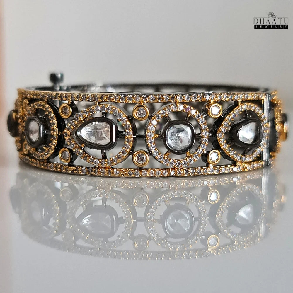 Front view of Dhaatu Jewelry Polki Kundan Inspired Black Rhodium Plated Gold Tone CZ Bangle Kada Bracelet on a reflective white surface, showing off its full design.