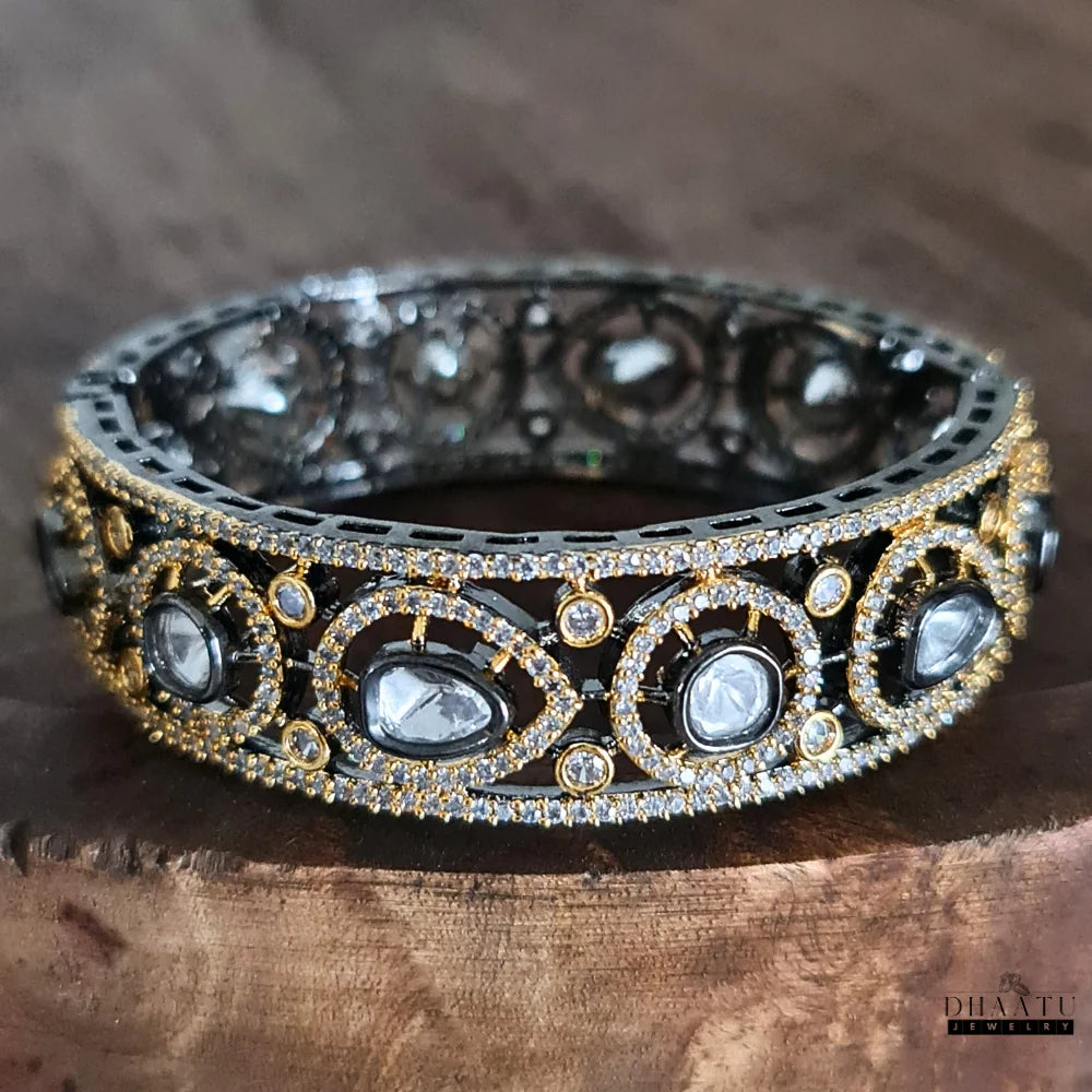 Dhaatu Jewelry Polki Kundan Inspired Black Rhodium Plated Gold Tone CZ Bangle Kada Bracelet displayed on a rustic wooden surface, accentuating its rich tones.