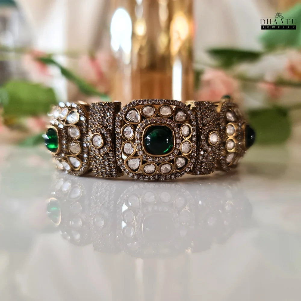Front angled view of a Dhaatu Jewelry Polki and Emerald Kada Bracelet, emphasizing the vibrant emerald stones and detailed setting.