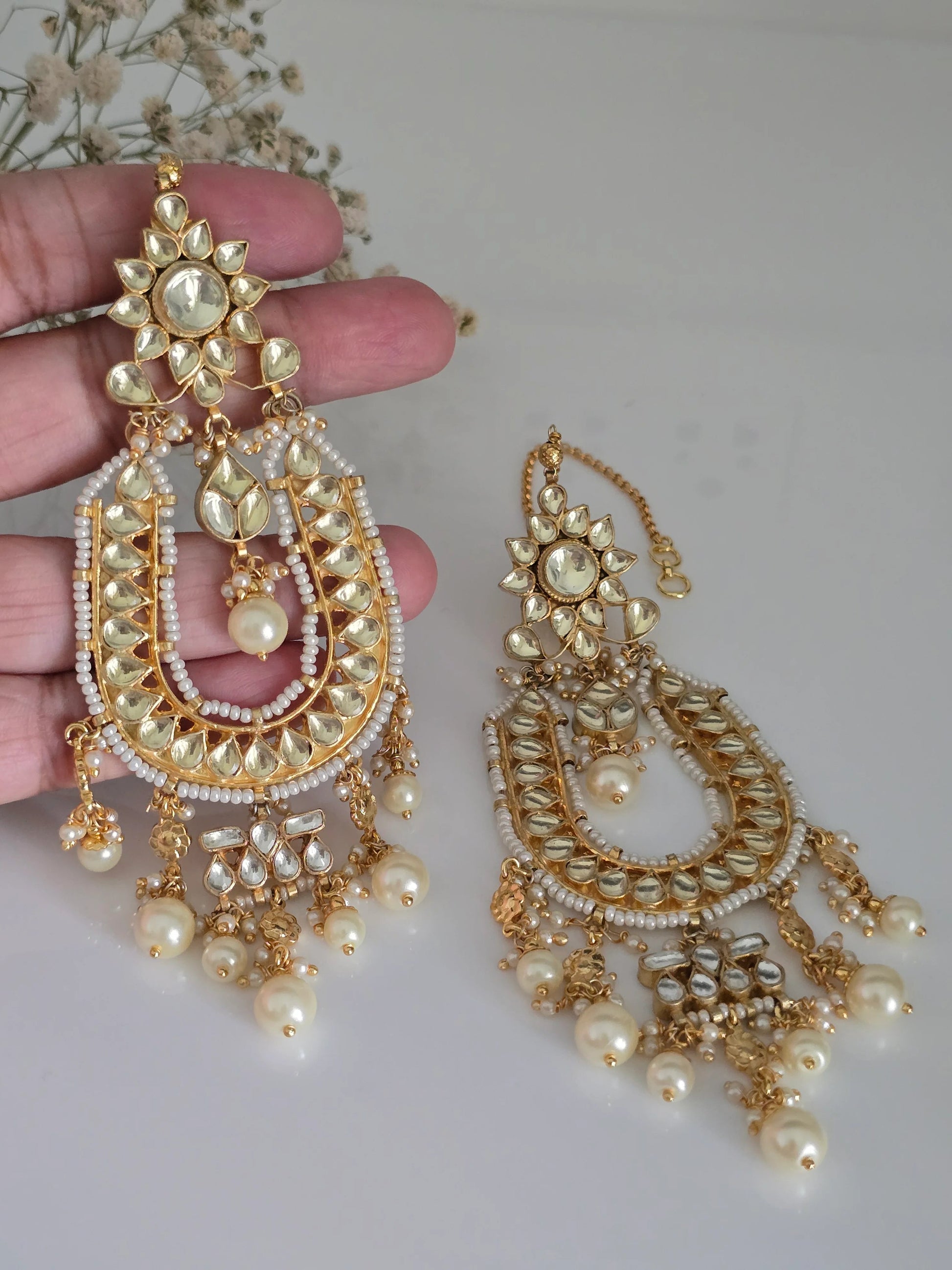 Close-up of gold-plated Kundan and pearl Chandbali earrings being held, highlighting the intricate details and pearl drops.