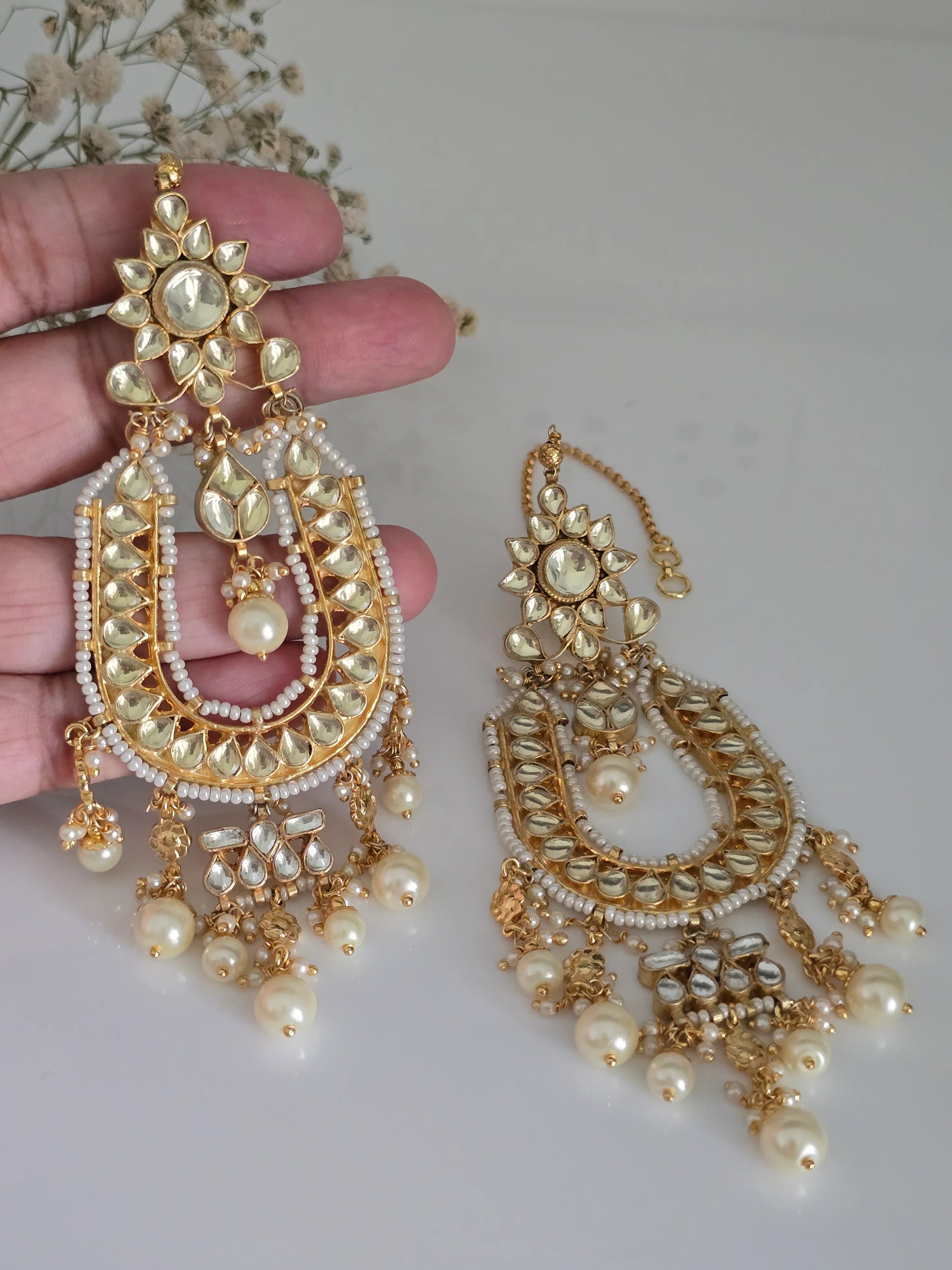 Close-up of gold-plated Kundan and pearl Chandbali earrings being held, highlighting the intricate details and pearl drops.