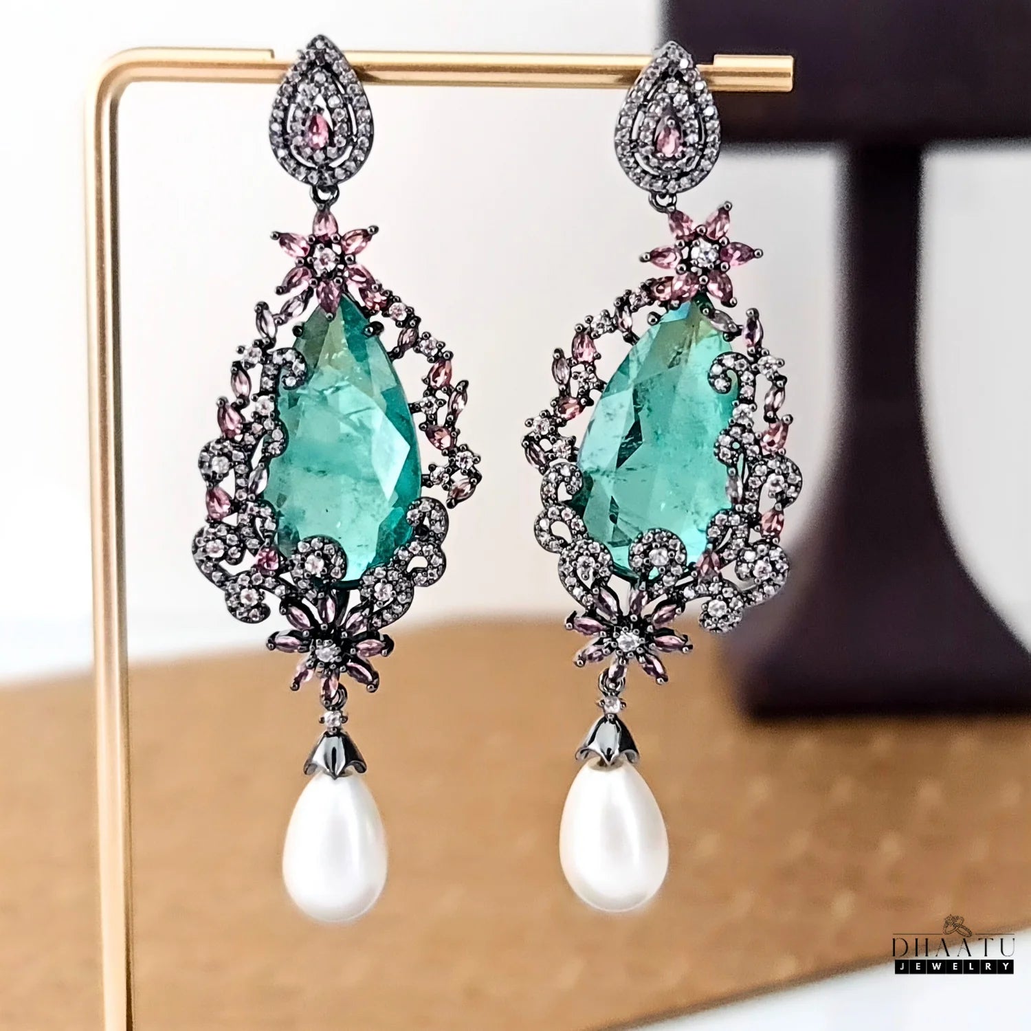 DHAATU JEWELRY green doublet stone and pearl drop earrings displayed on a gold stand.
