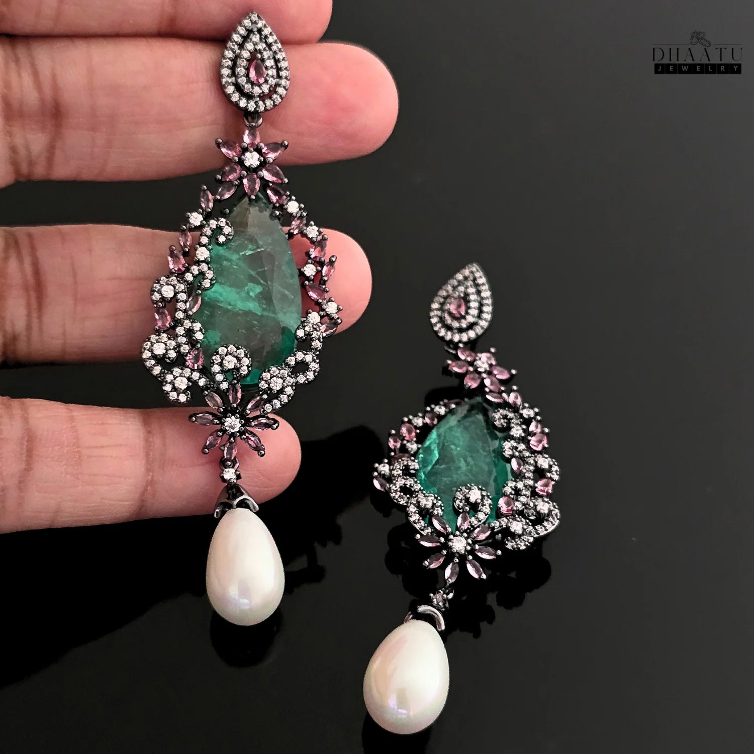 Hand holding one of the DHAATU JEWELRY green AD stone and pearl drop earrings for size reference.