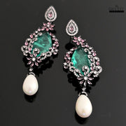 Close-up shot of DHAATU JEWELRY green AD stone and pearl drop earrings on a black reflective surface.