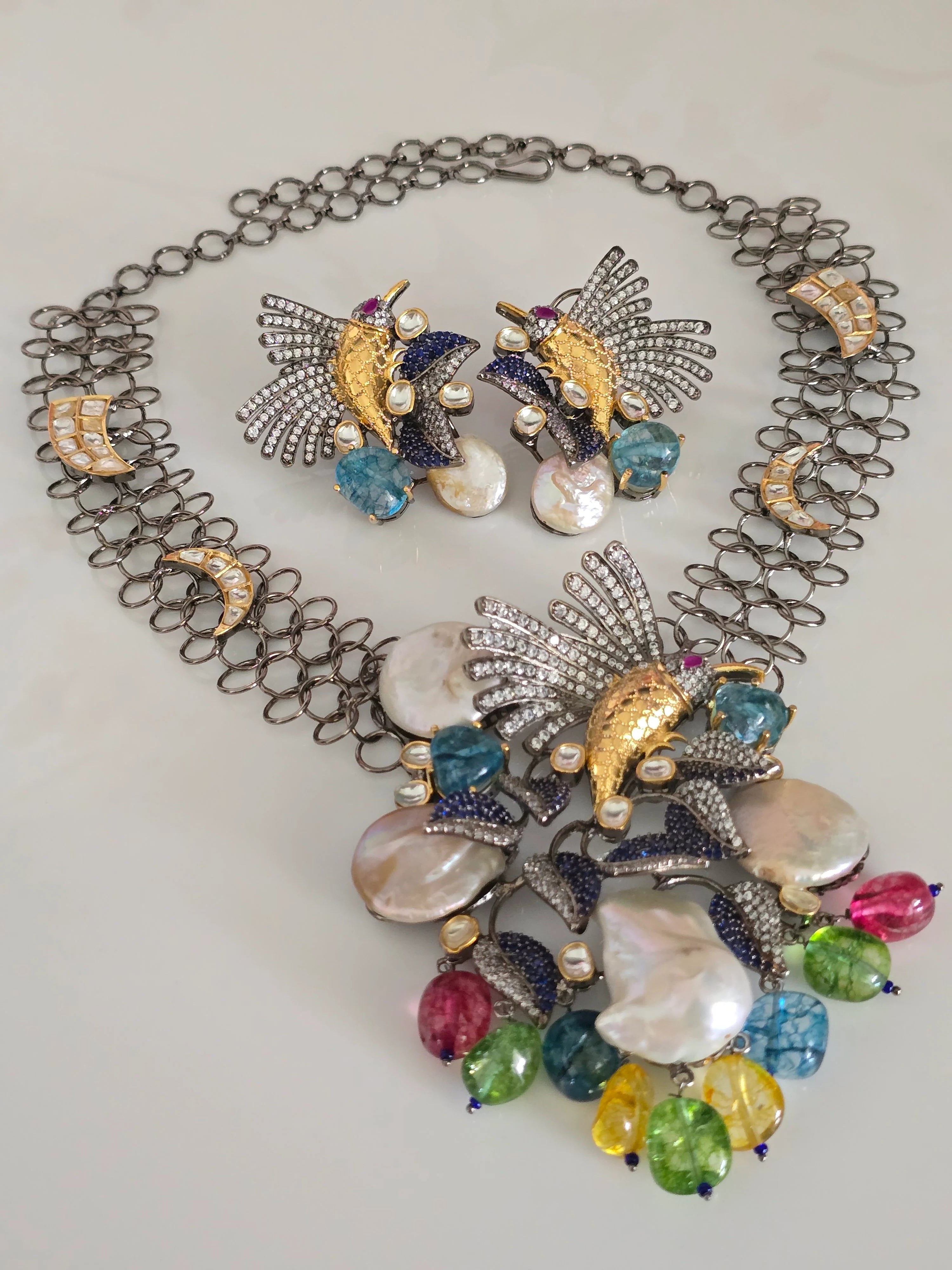 Full view of an artificial jewelry set featuring a hummingbird necklace with baroque pearls and colorful beads, and matching hummingbird earrings, on a white background.