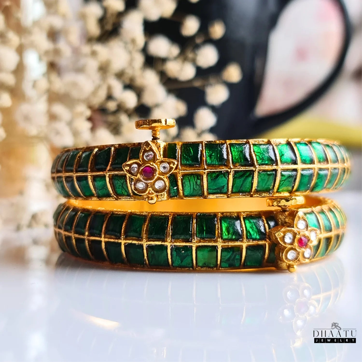 Pair of gold-plated traditional Indian Jadau kada bangles featuring rich Kemp emerald green square-cut stones and an intricate floral clasp.