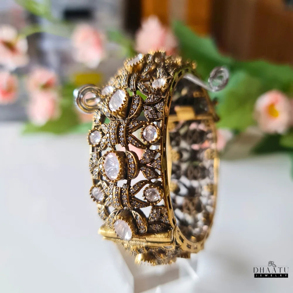 Side angle view of the gold-plated kada bracelet on a display stand, highlighting the design and stones.