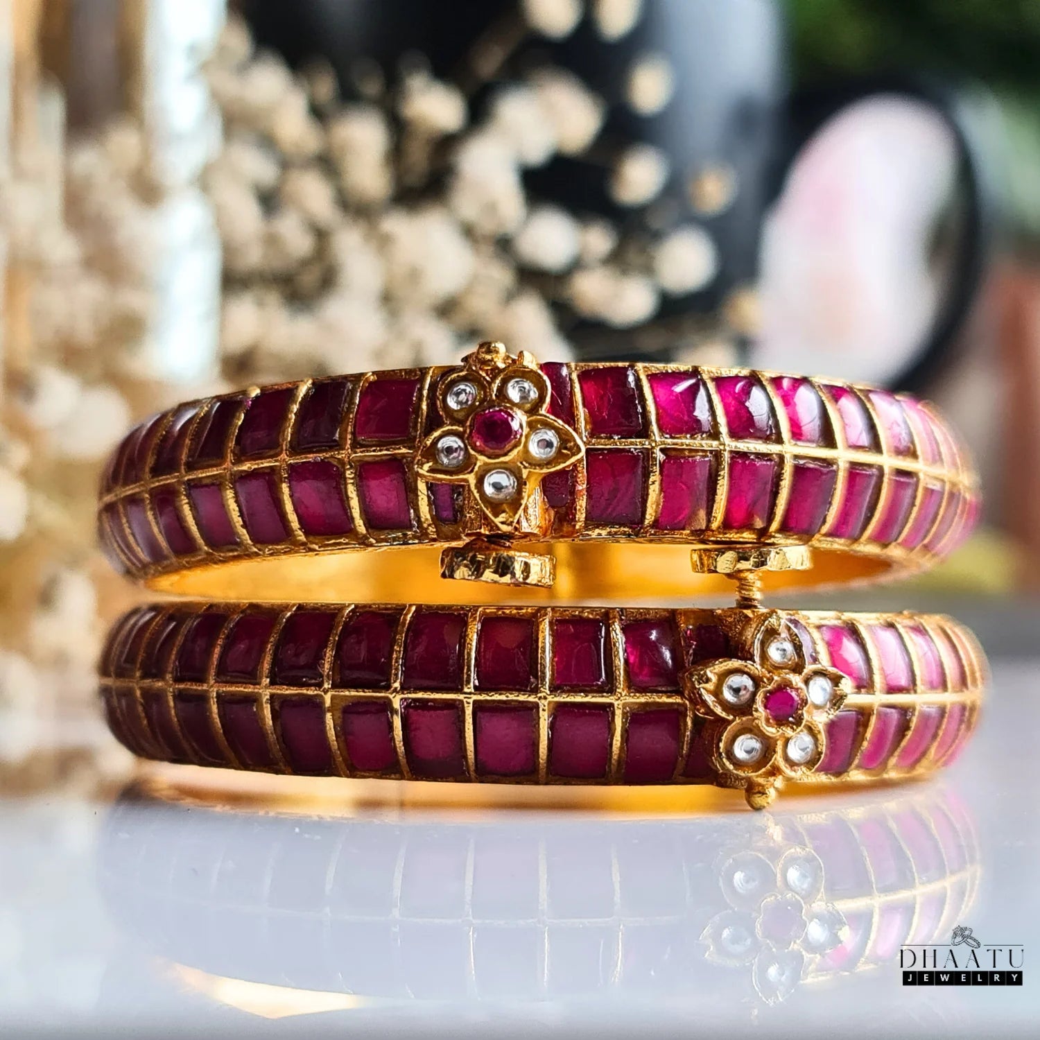 Close-up of a pair of gold-plated traditional Indian Jadau kada bangles featuring vibrant Kemp ruby red square-cut stones and a floral clasp with white and red accents.
