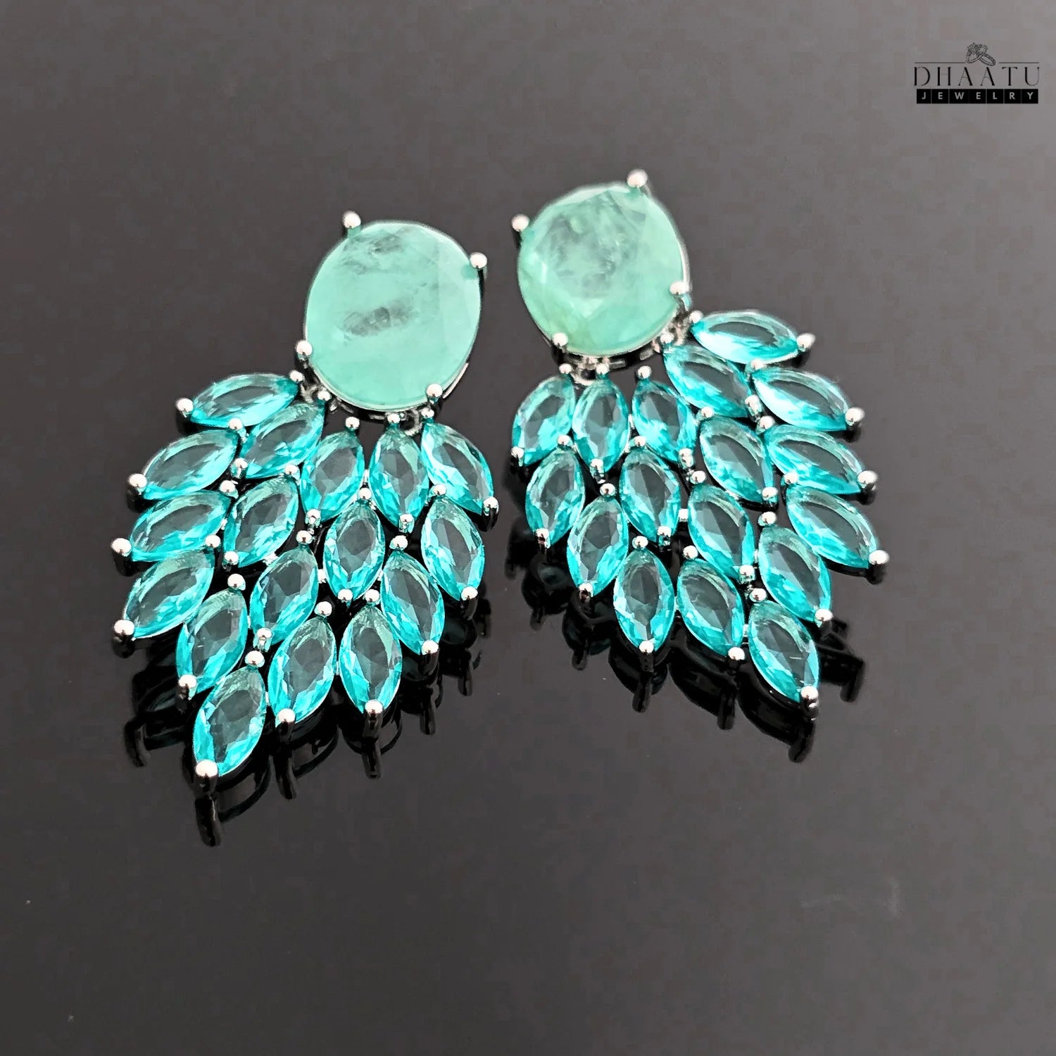 A view of the Aqua Chalcedony and marquise cut blue stone dangler earrings on a reflective dark surface, emphasizing their brilliant blue color and design.