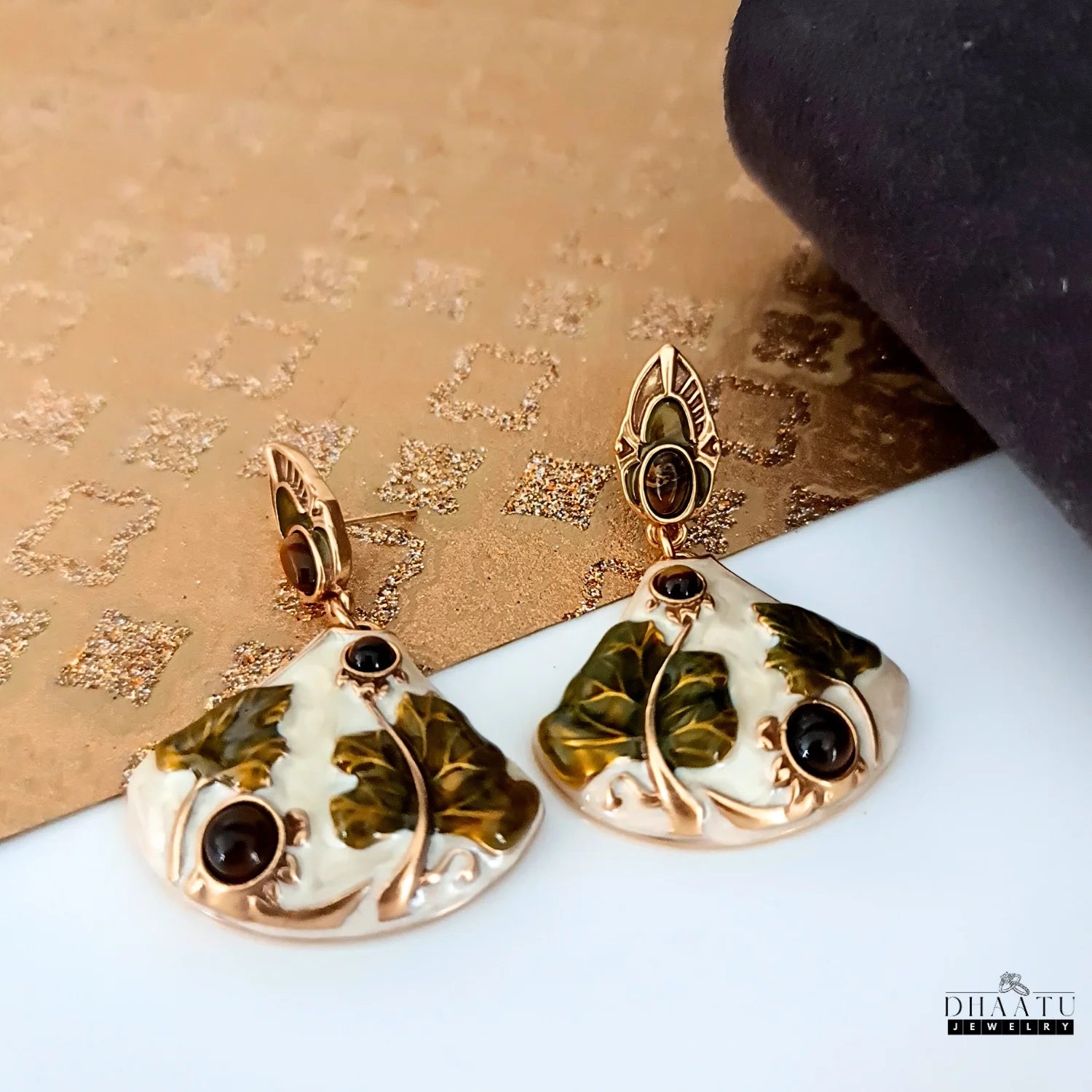 Elegant Art Nouveau lotus earrings with tiger's eye stones, photographed on a textured gold and white background.