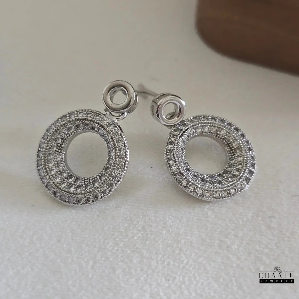 Pair of artificial zircon-studded circle drop earrings from Dhaatu Jewelry resting on a clean white surface.
