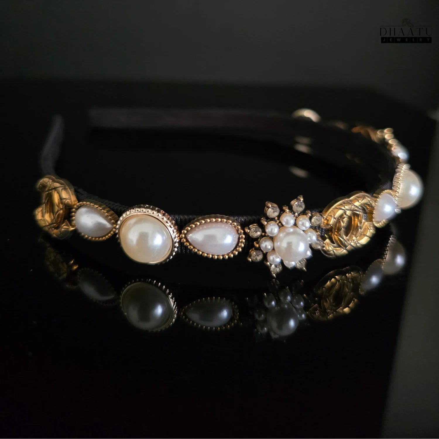 Close-up shot of a black and gold artificial hairband with faux pearls, crystals, and gold accents, showing reflection on a dark surface