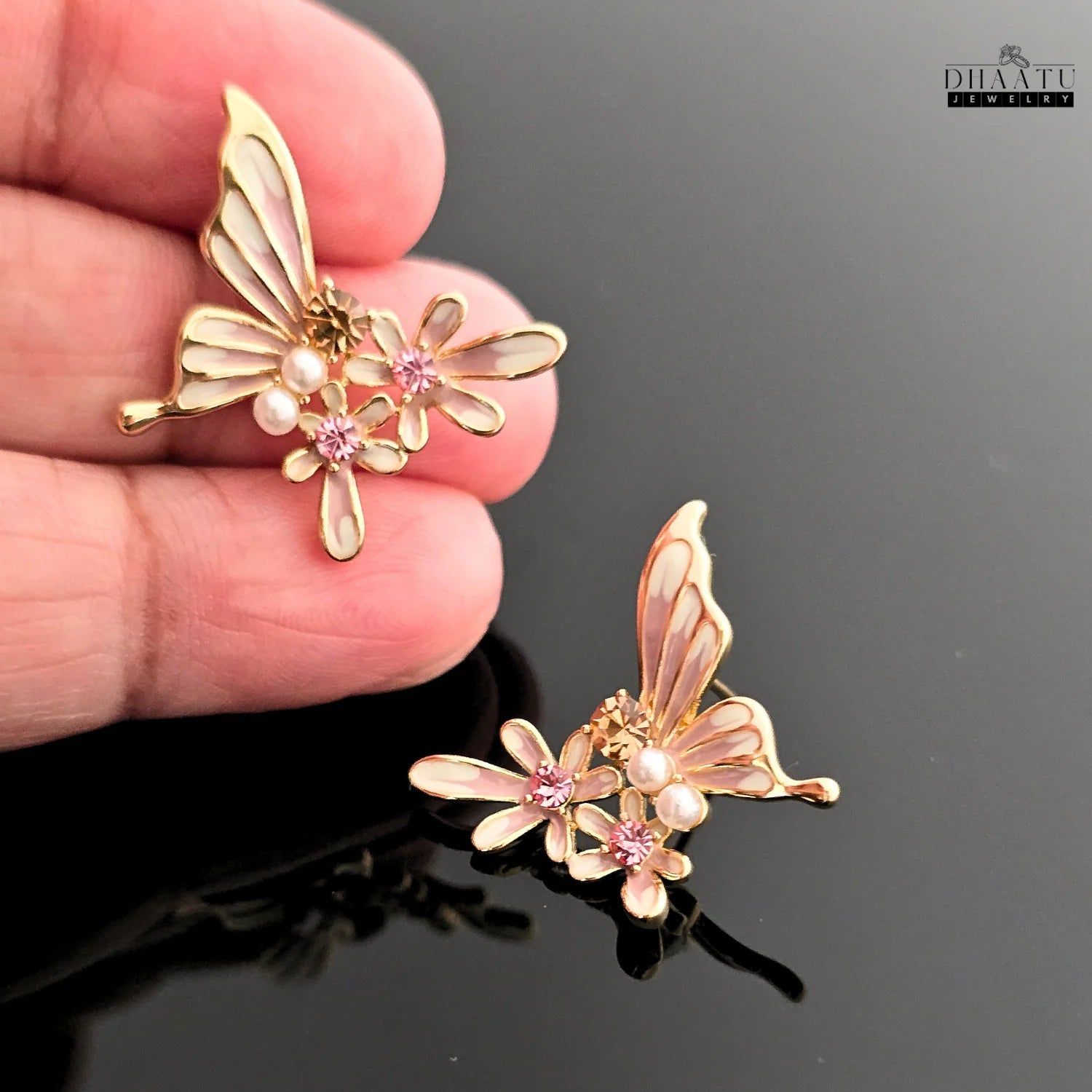 Close-up of a hand holding a pink and white butterfly and flower earring to show scale.