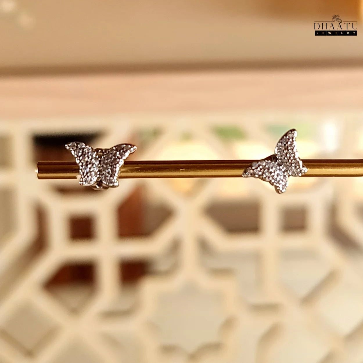 Two sparkling butterfly stud earrings with zircon stones, showcased on a golden rod against a blurred background.


