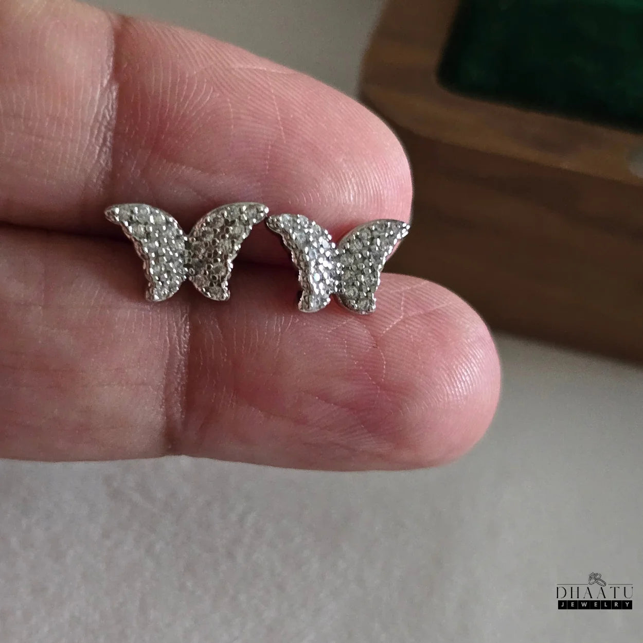 Silver-toned butterfly stud earrings, intricately detailed with zircons, held delicately in a hand to show scale.