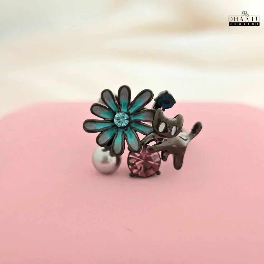 The adjustable ring with a playful cat and floral design, displayed on a pink surface to highlight the colorful details and craftsmanship of the piece.
