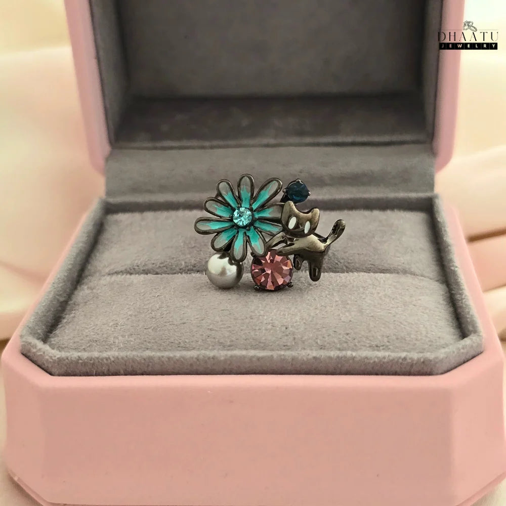 The DHAATU JEWELRY adjustable ring with a playful cat and flower design, presented in a pink and grey jewelry box.