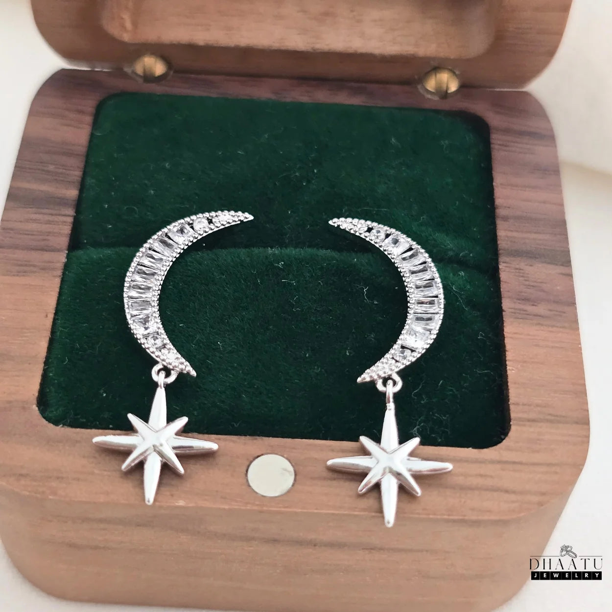 Celestial moon and star dangle earrings displayed in an open wooden jewelry box, showcasing their elegant design