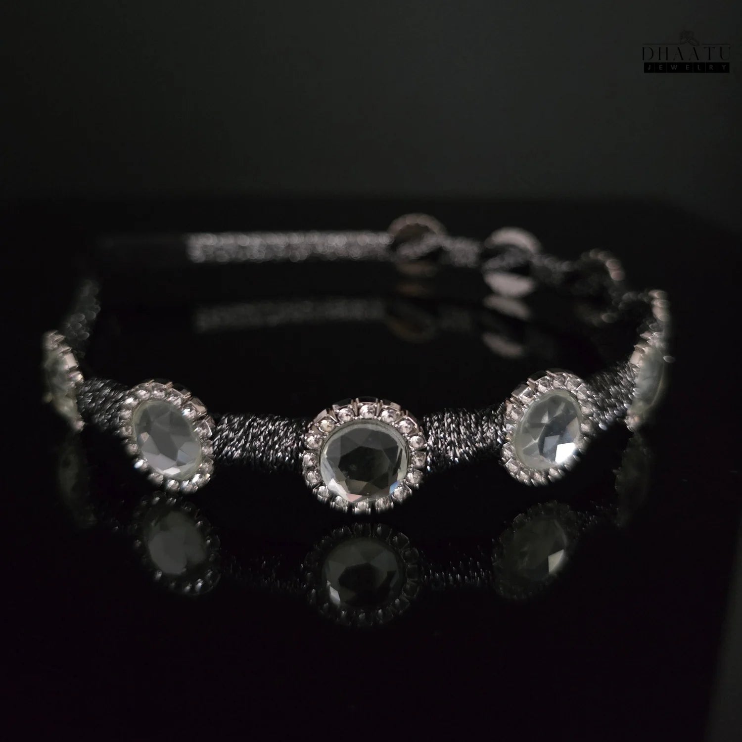 Chic black braided crystal headband with reflections on a dark surface, emphasizing the clear stones