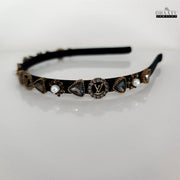 Full view of a chic black hairband with sparkling crystal designs and faux pearls on a white background