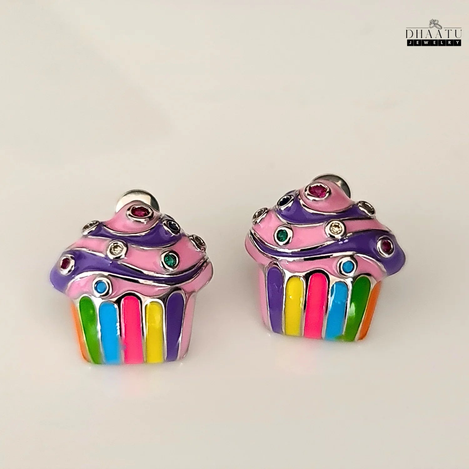 A pair of colorful cupcake enamel stud earrings from DHAATU JEWELRY on a clean white background, showcasing the vibrant rainbow stripes and rhinestone details.