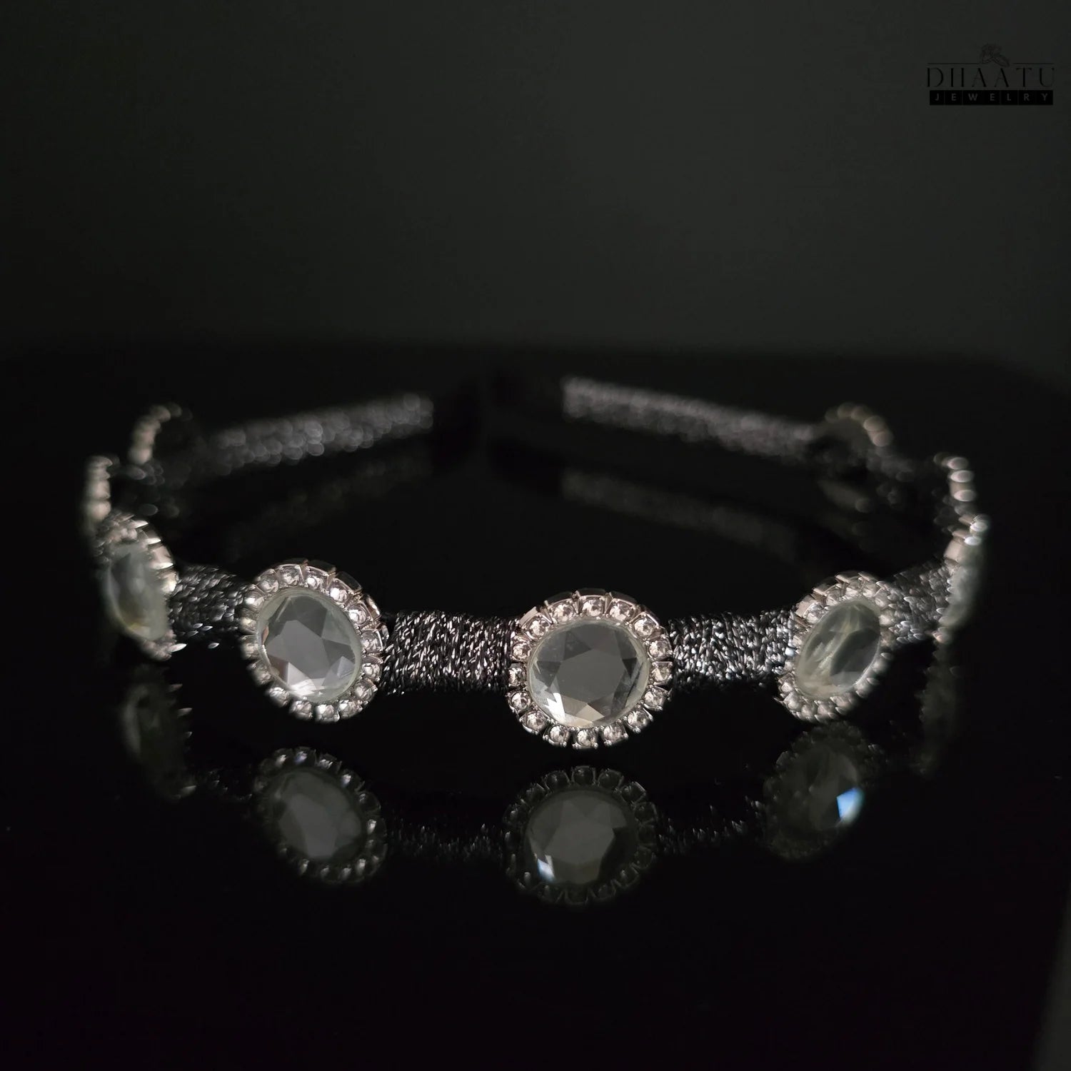 Contemporary crystal hairband with a black braided band, presented in a dark setting with subtle reflections.