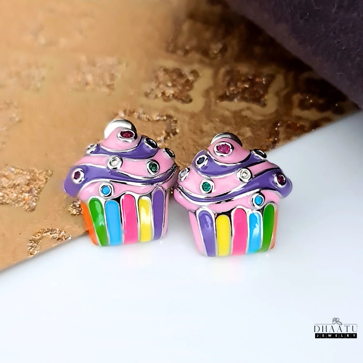 Colorful cupcake stud earrings displayed on a textured background, suggesting a party or fun occasion, emphasizing the colorful design and rhinestones.