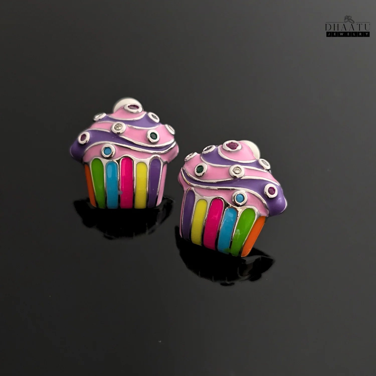 Colorful cupcake stud earrings on a reflective black surface, highlighting the glossy enamel and intricate details.