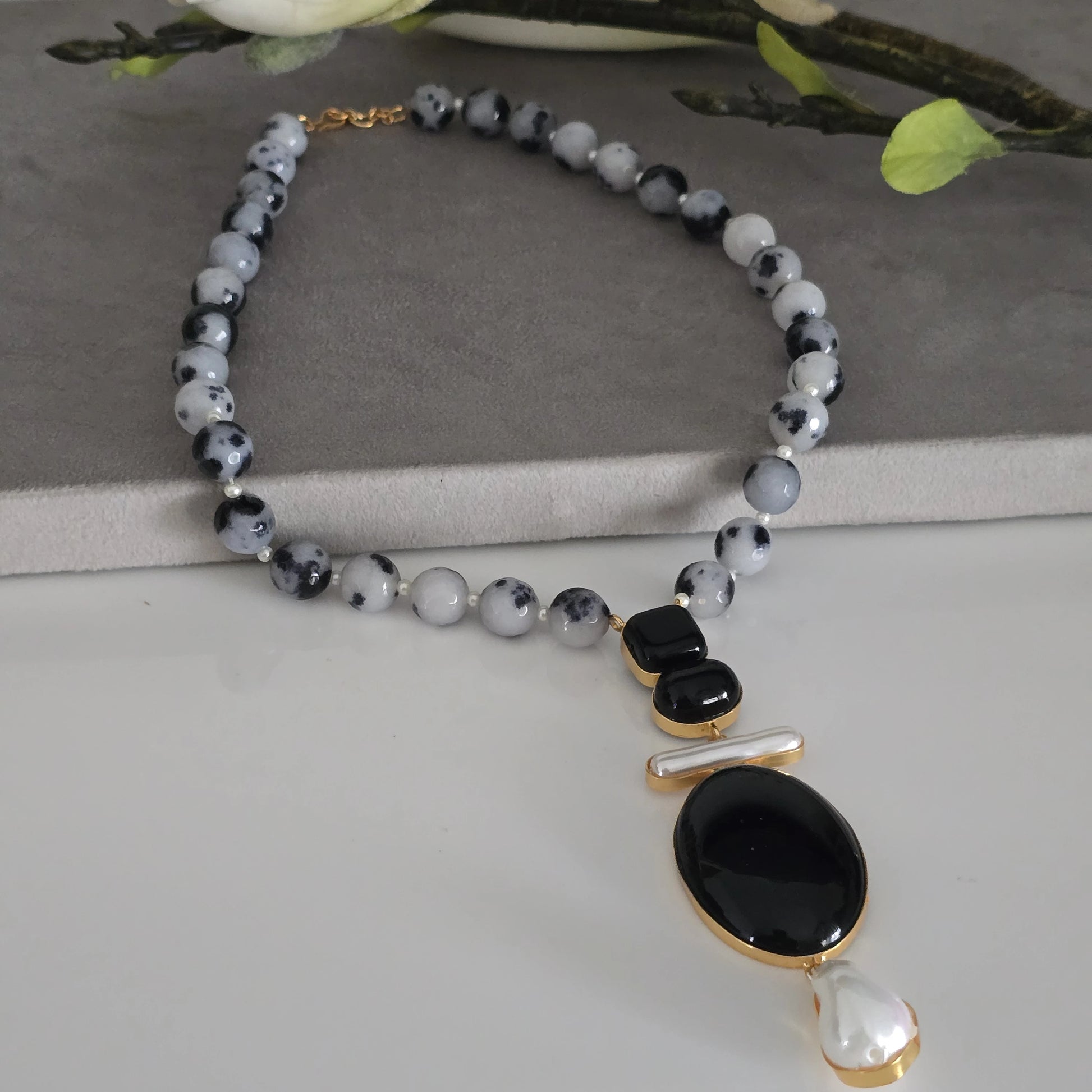 Handcrafted black and white dalmatian jasper beaded necklace with unique black stone and pearl drop pendant, natural stone statement jewelry for women on a white bg