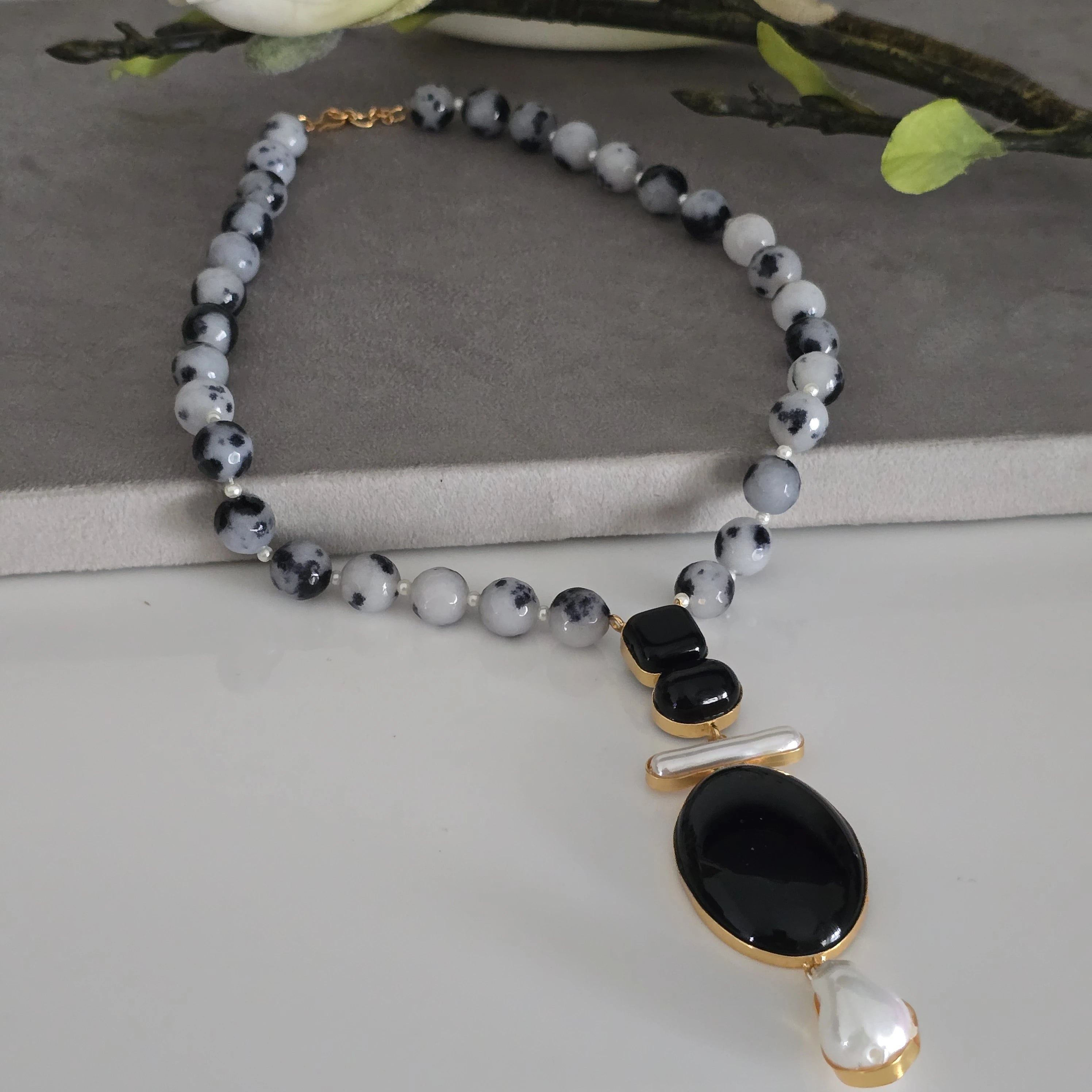 Handcrafted black and white dalmatian jasper beaded necklace with unique black stone and pearl drop pendant, natural stone statement jewelry for women on a white bg