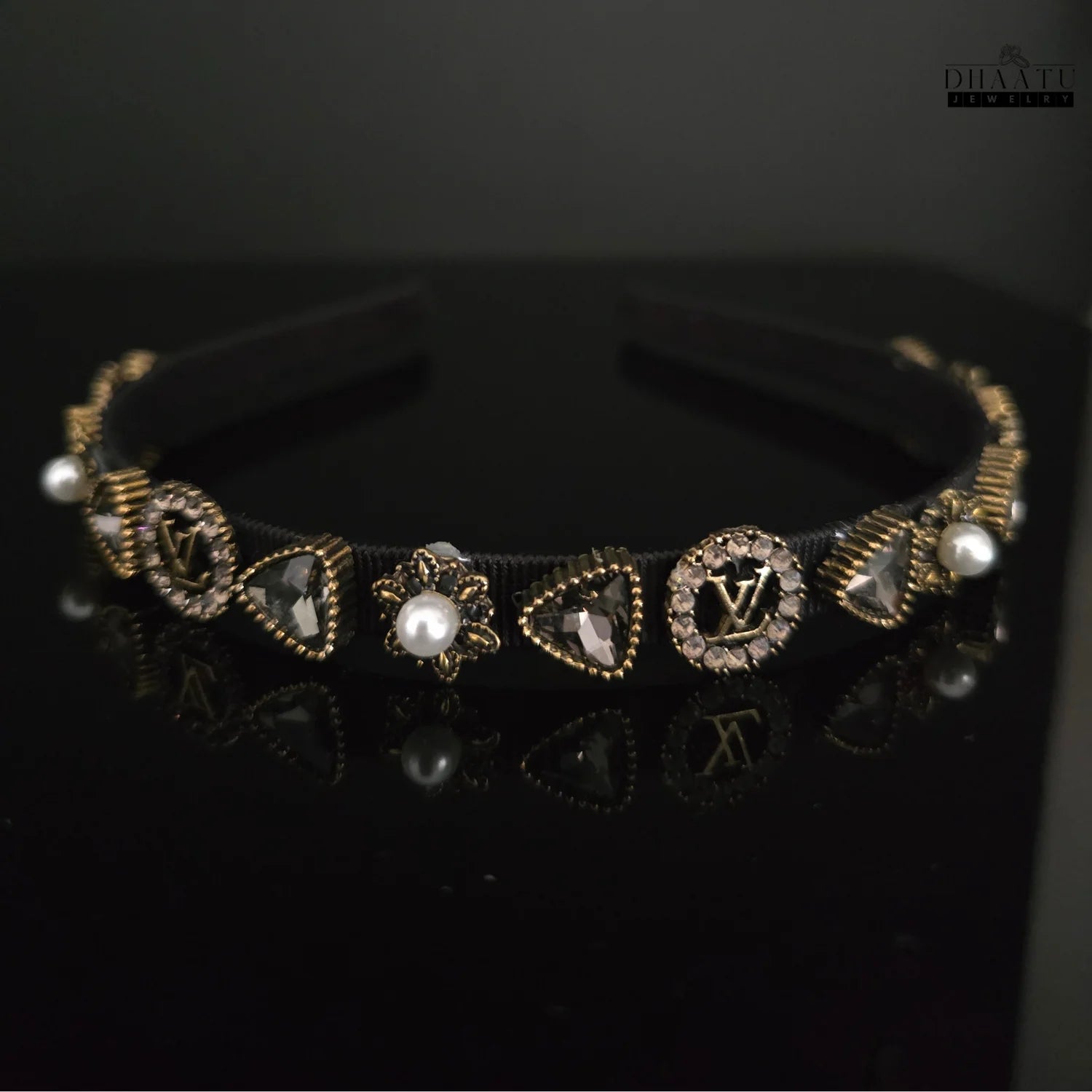 Close-up front view of a designer-inspired black hairband with gold-toned crystal accents and faux pearls.

