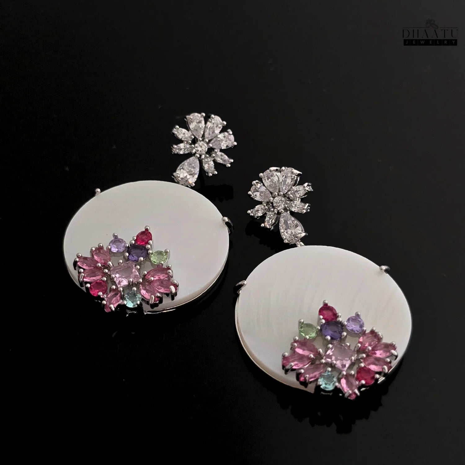 Close-up of Dhaatu Jewelry floral stud dangle earrings with cubic zirconia and multi-colored stones against a black background.