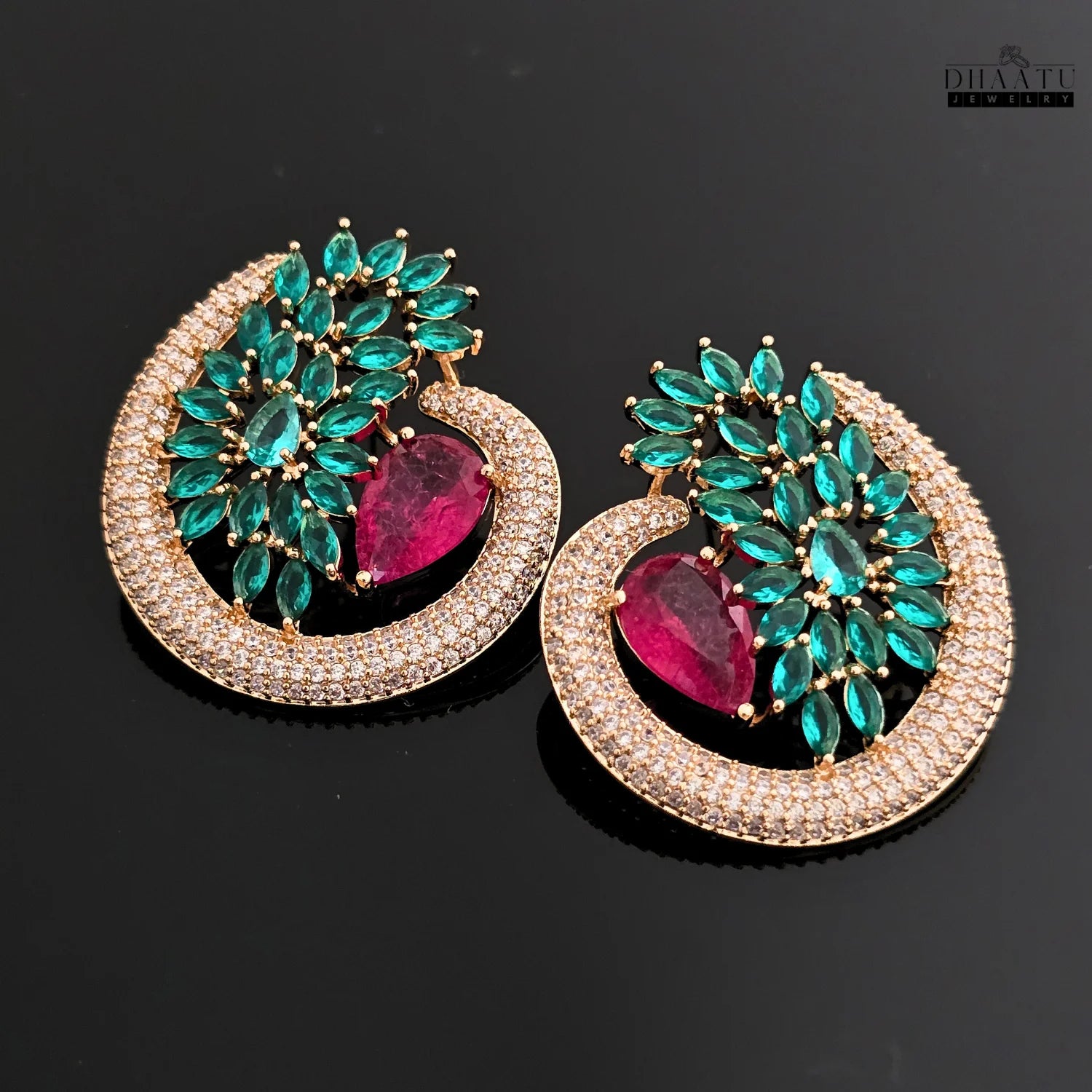 A pair of Dhaatu green and ruby CZ stone stud earrings placed on a black background, offering a clear view of the teardrop and marquise-cut stones.