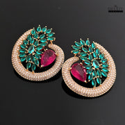 A pair of Dhaatu green and ruby CZ stone stud earrings placed on a black background, offering a clear view of the teardrop and marquise-cut stones.