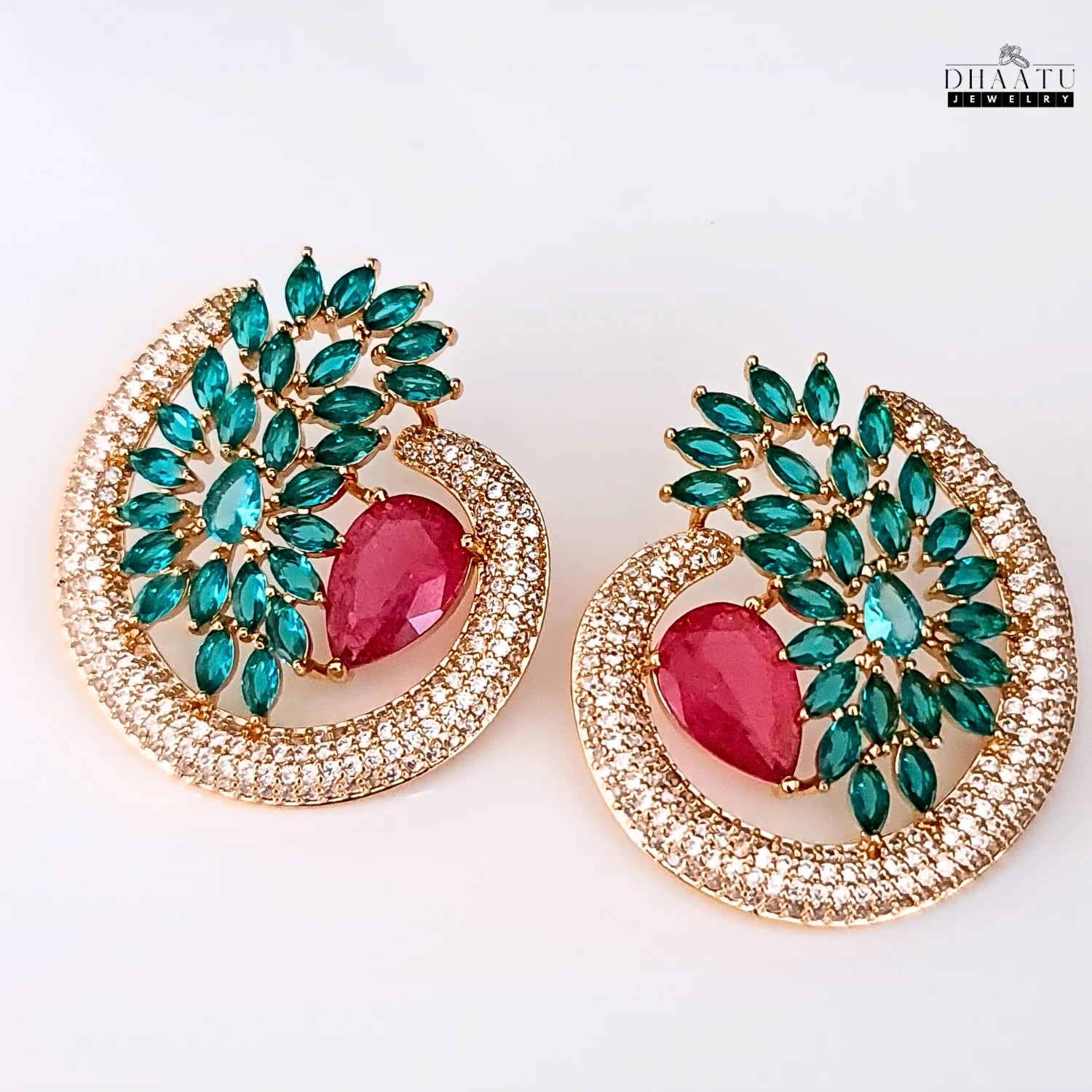 A pair of Dhaatu green and ruby cubic zirconia (CZ) stone stud earrings on a white background, showcasing the intricate details of the design and sparkling stones.