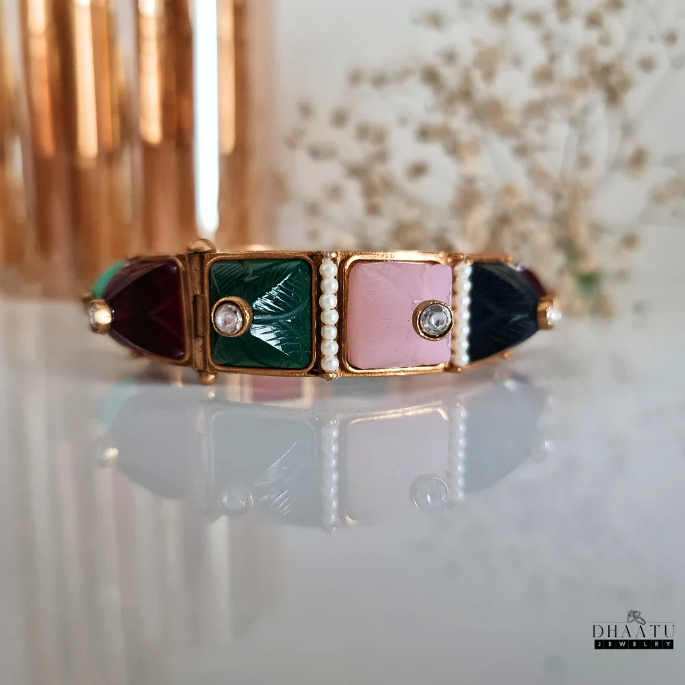 Another angled view of a multicolor carved stone and pearl kada bracelet on a display stand, focusing on the pink, green, maroon, and turquoise carved stones.
