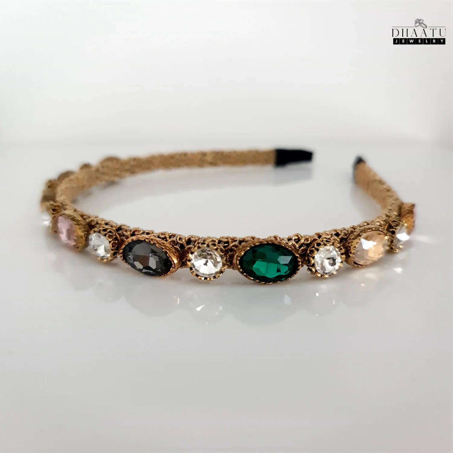 Full view of Dhaatu Jeweled Headband on a white background, showcasing the array of multi-color gemstones including green, pink, charcoal, and clear stones on a textured gold-toned band