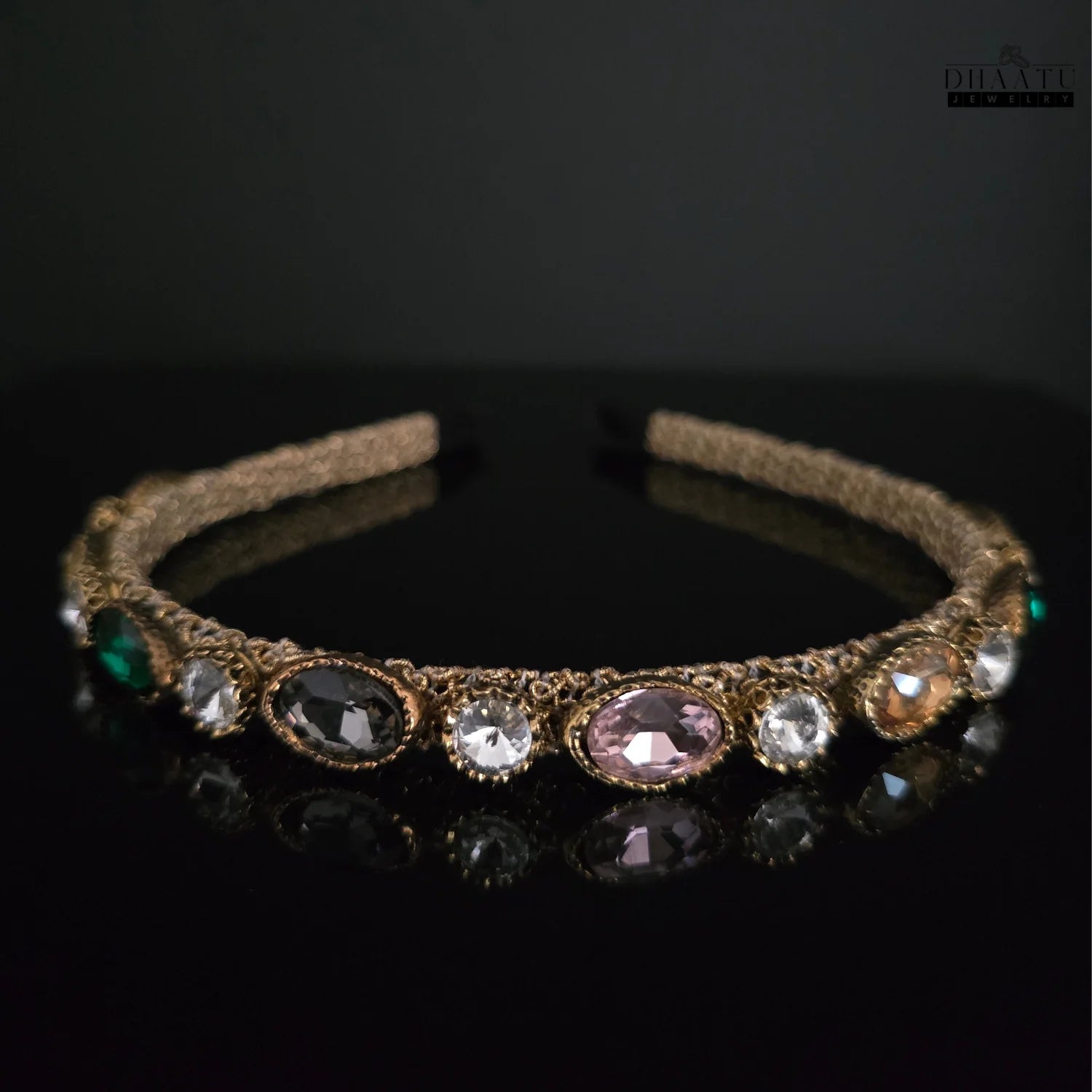 Dhaatu Jeweled Headband featuring a central pink gemstone surrounded by clear, charcoal, green, and peach accent stones on a gold-toned band