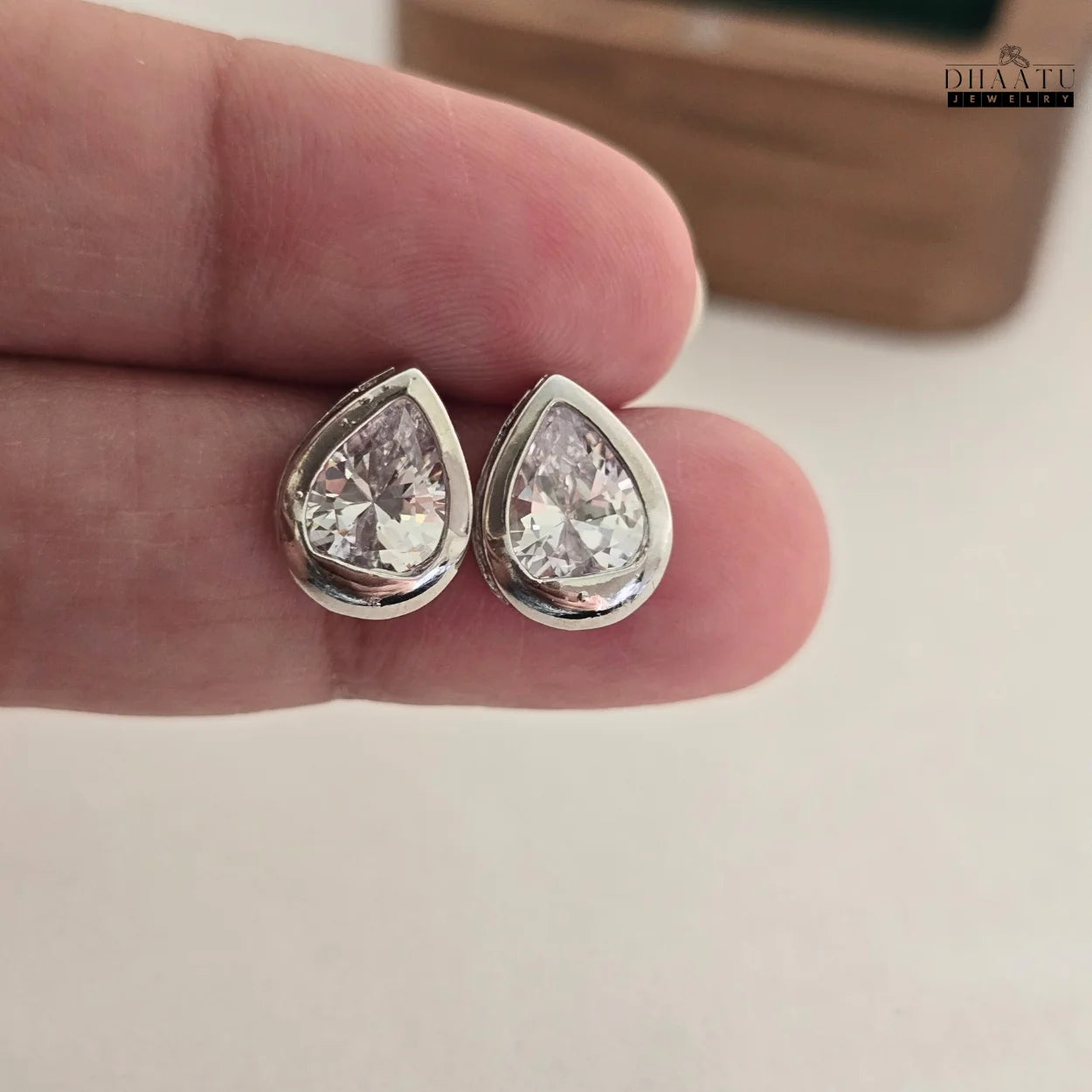Closeup of DHAATU JEWELRY pear-cut American diamond stud earrings held in hand, showcasing intricate details and brilliant sparkle