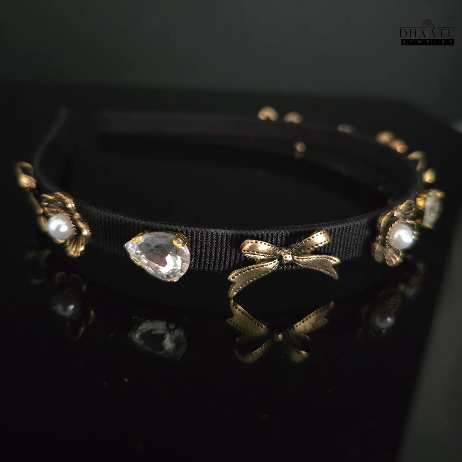 Close-up of Dhaatu Jewelry black and gold embellished hairband with pearl and crystal details on a dark surface.