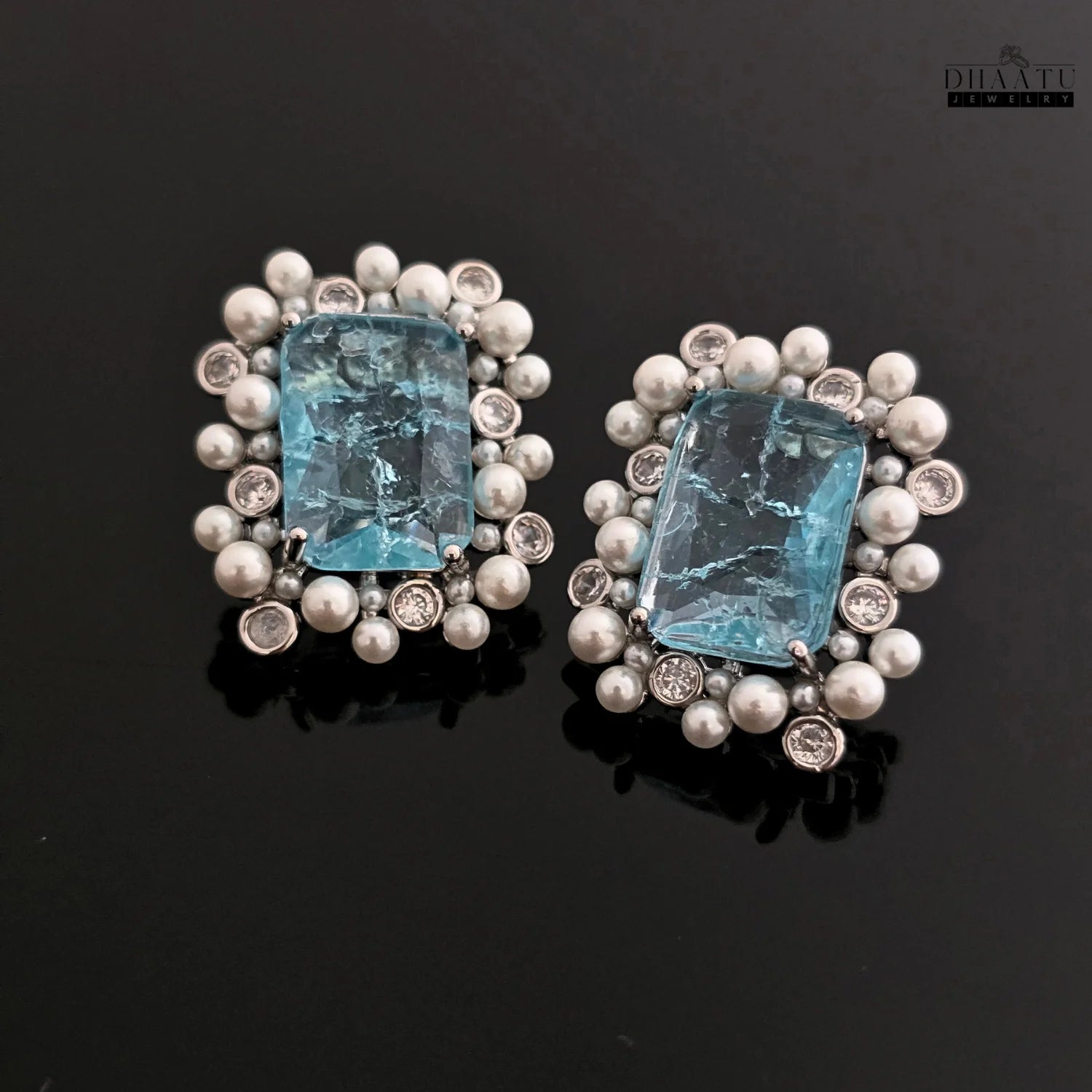 Pair of earrings with blue gemstones and pearl-like elements on a dark background