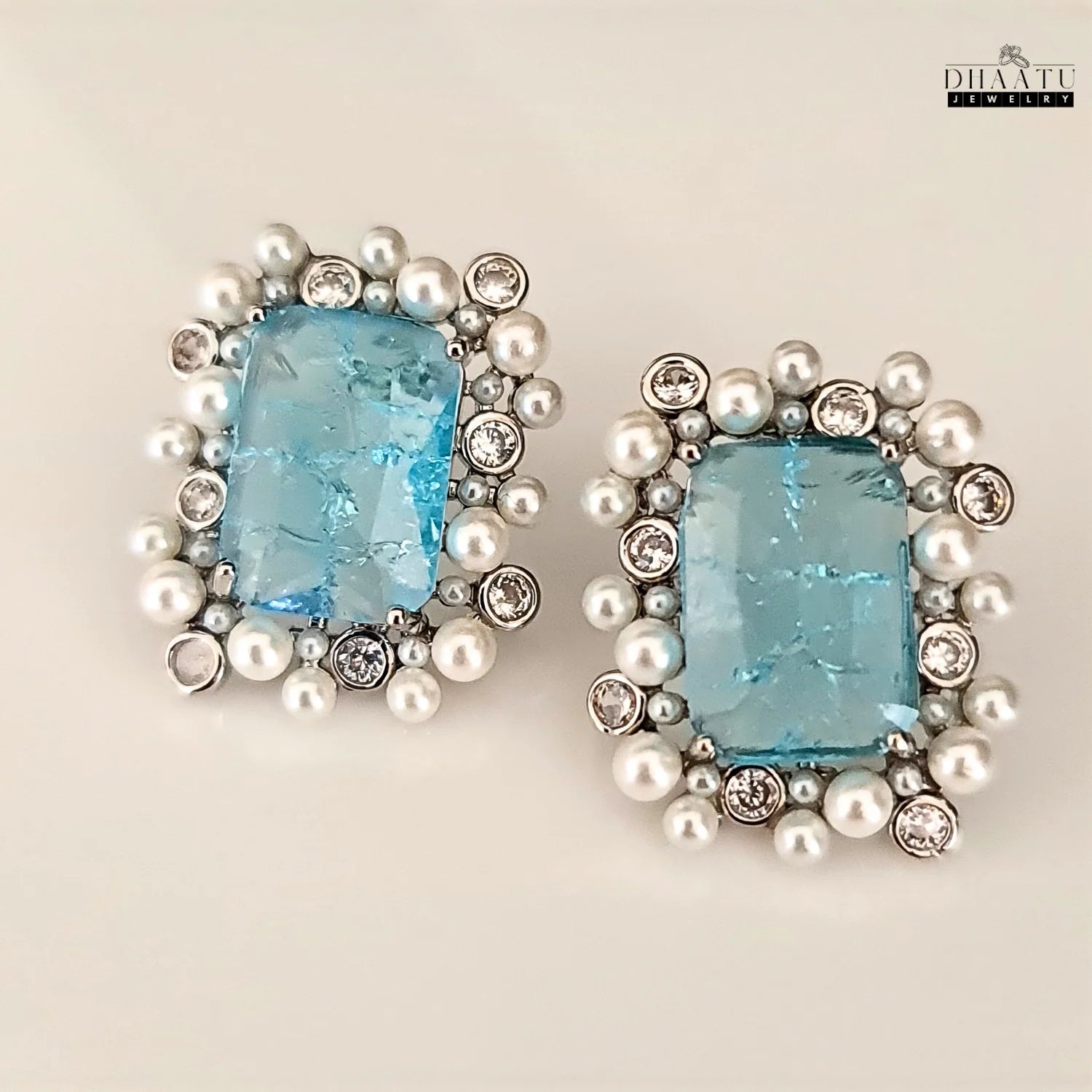 Pair of earrings with blue gemstones and pearl-like beads on a beige background