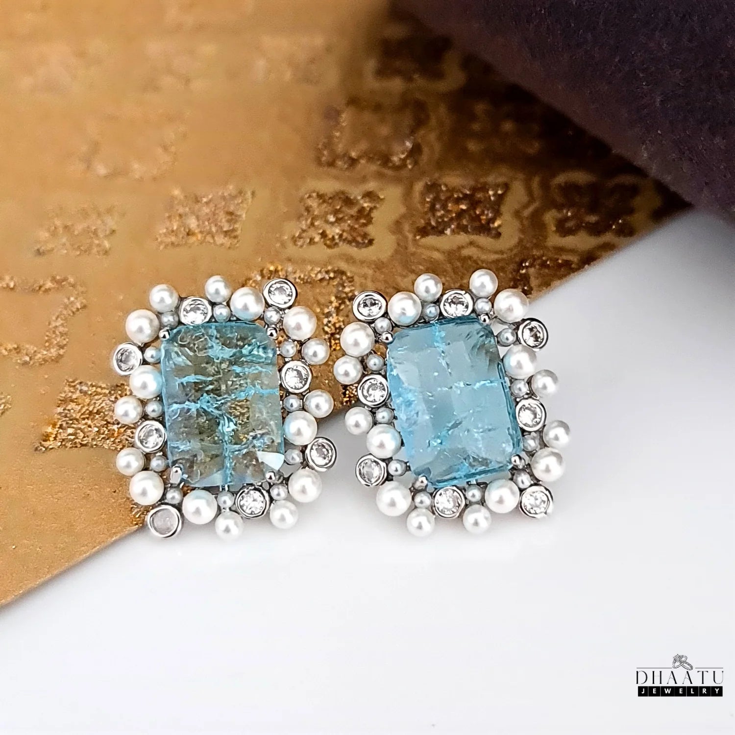 Pair of earrings with blue gemstones and pearl-like accents on a textured surface.