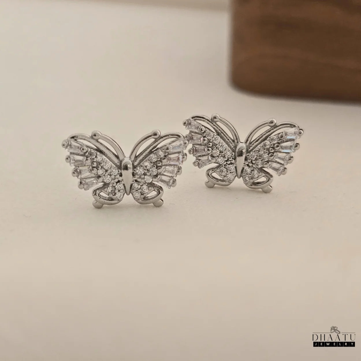 Pair of Dhaatu Jewelry silver butterfly stud earrings with zircon stones on a clean white background.