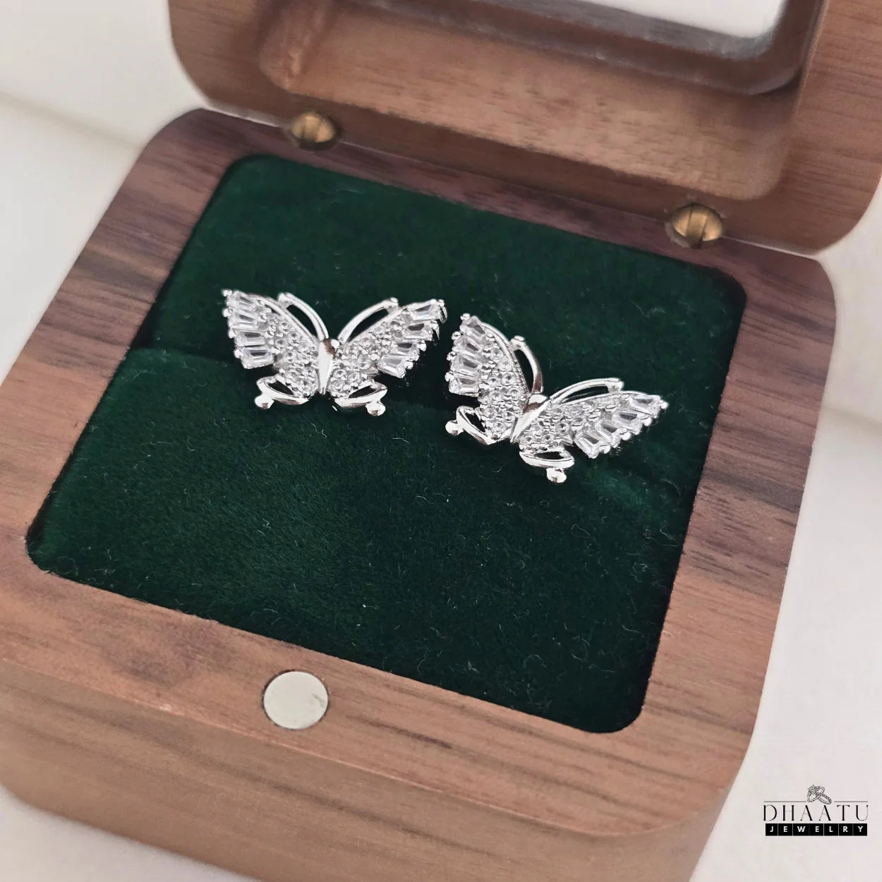 Dhaatu Jewelry silver butterfly stud earrings with zircon stones displayed in a wooden gift box with a green velvet interior.